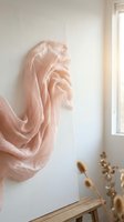 Flowing peach silk fabric draped against white wall in minimalist interior with natural light and dried flowers creating elegant textile art composition.