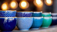 Colorful ceramic bowls in blue and turquoise with dotted patterns arranged in row, soft bokeh lights in background create cozy atmosphere. Perfect for home decor.