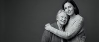 Young woman embracing elderly mother in warm hug against gray background. Intergenerational love, family bonding, caregiving concept for healthcare campaigns.