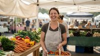 Happy female farmer selling fresh organic vegetables at outdoor farmers market stand with colorful produce display for healthy local food business.