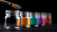 Paint brush dipping into glass jar with vibrant orange paint, row of colorful paint jars blurred in background on dark surface, artistic composition.
