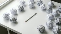 Crumpled paper balls surrounding a pencil on a white desk, symbolizing creative struggle, writer's block, and brainstorming process in business or education.