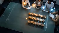 Business team discussing mission vision values strategy during corporate meeting with wooden letter blocks on glass table from above.