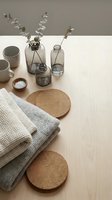 Minimalist home decor flat lay with eucalyptus branches in glass vases, knitted textiles, cork coasters and ceramic cups on wooden surface for interior design.