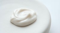 Creamy white cosmetic product swirl on white surface, skincare moisturizer or lotion texture for beauty and wellness applications.