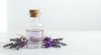 Lavender essential oil in glass bottle with cork stopper surrounded by fresh purple lavender flowers on white background for aromatherapy and wellness.