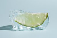 Lime slice frozen inside a clear melting ice cube on a light blue background, fresh citrus concept for summer drinks and food.