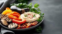 Grilled vegetables and hummus dip served on dark plate with fresh herbs. Colorful bell peppers, mushrooms and eggplant slices create healthy appetizer platter.