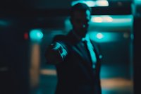 Young African American man in dark environment illuminated by atmospheric cyan neon lights, holding cigarette with rising smoke creating moody nightlife scene.
