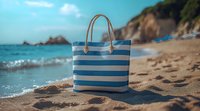 Striped blue and white beach bag with rope handles on sandy beach near ocean waves and rocky coastline, summer vacation lifestyle composition.