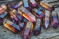 Colorful amethyst and citrine crystal points scattered on rustic wooden surface, displaying vibrant purple and golden hues in natural lighting.