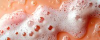 Soap foam and bubbles on coral pink background with water drops creating abstract macro texture pattern with soft light and shadows.