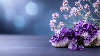 Purple amethyst crystal cluster with delicate pink flowers against blurred blue bokeh background, creating mystical healing atmosphere for wellness and spiritual concepts.