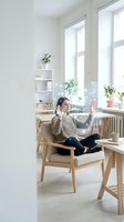 Young Asian woman having video call on laptop in bright modern home office with plants and wooden furniture for remote work and communication.