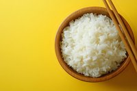 Steamed white jasmine rice in wooden bowl with chopsticks on vibrant yellow background, overhead view. Asian cuisine and food photography concept.