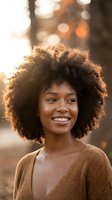 Happy young African American woman with natural curly afro hair smiling outdoors with warm golden hour lighting and bokeh background for lifestyle content.
