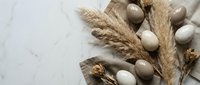 Natural Easter eggs in neutral beige and cream tones with dried pampas grass and cotton stems on marble surface for spring holiday decoration.
