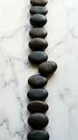 Stacked smooth dark stones arranged in vertical line on white marble surface, symbolizing balance, wellness, and mindfulness for spa and meditation concepts.