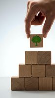 Hand placing wooden block with green tree icon on pyramid of natural wood cubes representing environmental growth and sustainable business development.