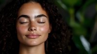Young Hispanic woman with curly dark hair and glowing natural skin smiling with eyes closed against green tropical leaves background, wellness and beauty concept.