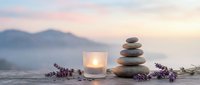 Zen meditation setup with balanced stone cairn, glowing candle and lavender sprigs against serene mountain landscape at peaceful sunset for wellness relaxation.