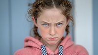 Young Caucasian woman with curly hair wearing pink hoodie showing serious determined expression for lifestyle and portrait photography.