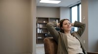 Young professional woman relaxing in office chair with hands behind head, taking break from work in modern workplace environment.