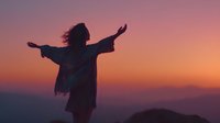 Silhouette of woman with arms outstretched against vibrant sunset sky over mountain landscape, expressing freedom and spiritual connection with nature.