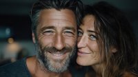 Happy mature couple embracing and smiling together in cozy indoor setting. Middle-aged man with beard and woman showing genuine affection and joy.