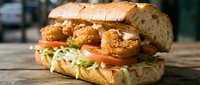 Crispy fried chicken sandwich with fresh lettuce and tomato on artisan bun, served on wooden table for restaurant menu and food advertising concepts.