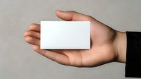 Hand holding blank white business card against neutral gray background, showcasing professional presentation for branding and corporate identity mockup.