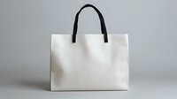 White shopping bag with black handles on neutral gray background, isolated mockup for retail branding and design presentation.