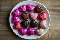 Colorful heart-shaped chocolates wrapped in foil arranged on white plate for Valentine's Day celebration and romantic occasions.