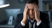 Stressed middle-aged Caucasian businessman in suit holding head in hands showing work pressure, mental fatigue and corporate burnout in office.
