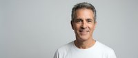 Confident mature Caucasian man with gray hair wearing white t-shirt smiling at camera on neutral background for business and lifestyle content.