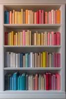 Colorful books arranged on white bookshelf with rainbow spectrum organization, creating vibrant home library display for interior design inspiration.