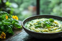 Homemade pesto pasta in rustic ceramic bowl with fresh basil leaves and yellow flowers on wooden table by window with garden view.