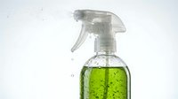 Spray bottle filled with bright green cleaning solution or disinfectant liquid, isolated on white background for household cleaning, sanitizing, and disinfection purposes.