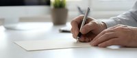 Close-up of male hands writing on blank white paper with pen at desk. Suitable for business, education, contract signing, note-taking, and office work concepts.