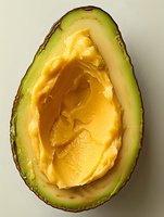 Fresh ripe avocado half filled with creamy yellow butter, creative food composition showing contrast between natural and dairy products on light background.