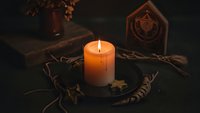 Mystical candle burning on wooden altar with tarot cards, crystals and occult symbols creating atmospheric fortune telling scene for spiritual practices.