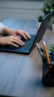 Hands typing on laptop keyboard at modern workspace with plants and office supplies on wooden desk for remote work and productivity.