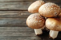 Fresh brown champignon mushrooms with water drops on caps arranged on rustic wooden background, macro food photography with selective focus.