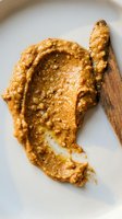 Creamy peanut butter spread on white plate with wooden knife, showing texture and consistency for cooking, baking, and food styling purposes.