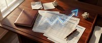 Wooden desk with financial documents, spreadsheets, and blue holographic chart overlay showing upward trend graph for business analytics and investment planning.