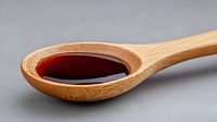 Red liquid in wooden bamboo spoon on gray background, close up view of natural organic sauce, condiment or syrup for cooking and food preparation.