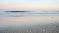 Serene coastal landscape at dawn with soft pink and blue tones reflecting on wet sand and calm ocean waves, ideal for travel and wellness backgrounds.