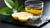 Whiskey glass with amber liquid on dark slate board alongside fresh lemon halves and green leaves creating elegant drinking scene for hospitality design.