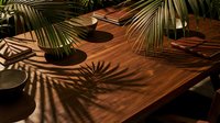 Wooden table with natural sunlight casting tropical palm leaf shadows, creating warm ambient lighting for interior design and home decor projects.