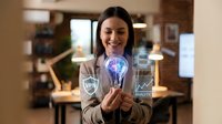 Professional Asian businesswoman holding glowing digital brain lightbulb with data analytics charts in modern office environment for innovation concepts.
